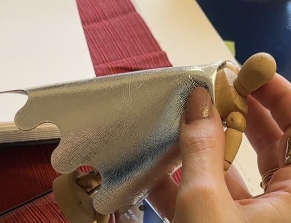 Mão de manequim de madeira segurando um tecido prata metálico de verdade